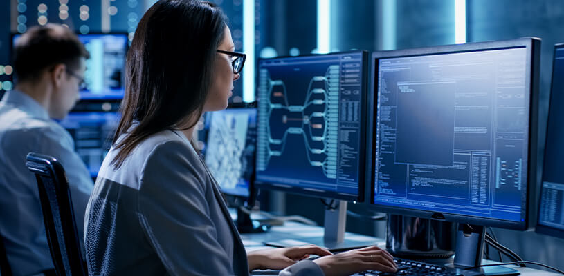 Woman and man behind computer monitors showing energy analytics and grid management results from energy simulation software.